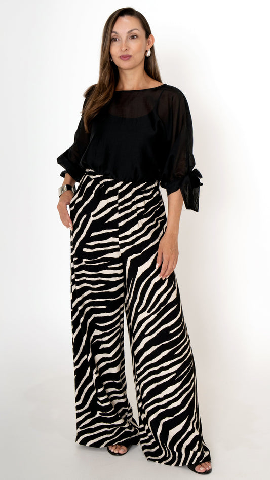 elegante ausgefallene Damenbekleidung in schwarz weiß: Modisch sommerliches Outfit bestehend aus einer weiten Zebra Print Hose und einer schwarzen Chiffonbluse mit Schleifen am Ärmel, Halbarm