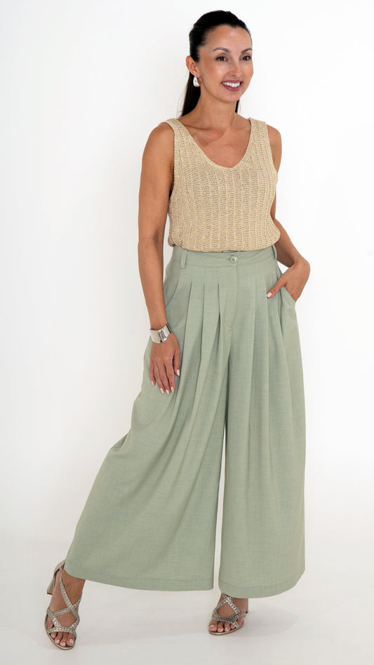 Elegante Damenbekleidung mit einem ausgefallenen Sommeroutfit. Es besteht aus einer verkürzten Stoffhose mit Falten und extra weitem Bein in einem hellen Maigrün. Das Oberteil ist ein goldenes Stricktop mit leichtem Glanz, ohne Ärmel