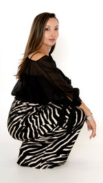 Moodbild in der Hocke: elegante ausgefallene Damenbekleidung in schwarz weiß: Modisch sommerliches Outfit bestehend aus einer weiten Zebra Print Hose und einer schwarzen Chiffonbluse  mit Schleifen am Ärmel, Halbarm