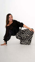 Fashion Editorial: elegante ausgefallene Damenbekleidung in schwarz weiß: Modisch sommerliches Outfit bestehend aus einer weiten Zebra Print Hose und einer schwarzen Volumen Chiffonbluse  mit Schleifen am Ärmel