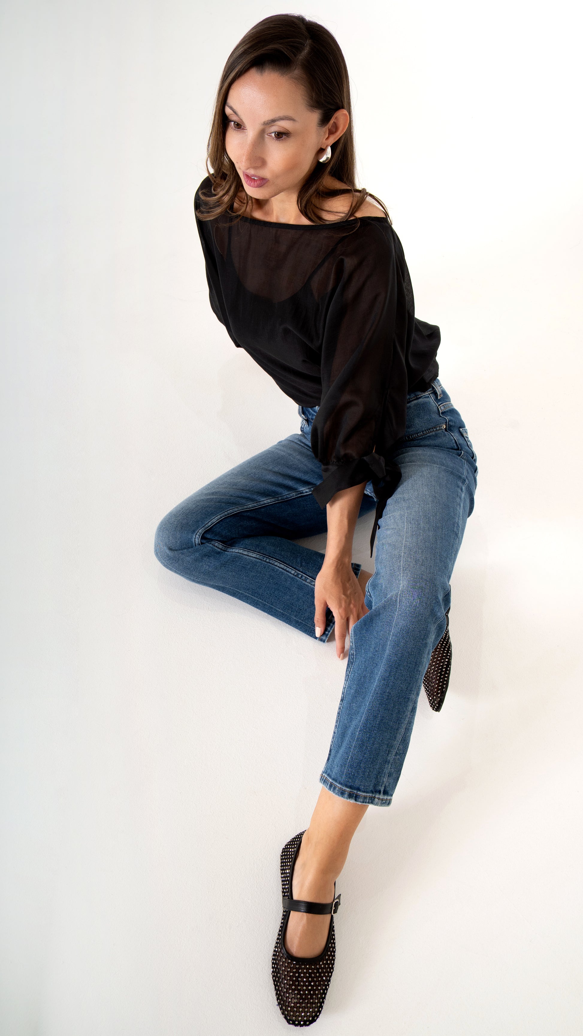 Feminine Damenkleidung sitzende Ansicht : gerade blaue Jeans verkürzt, schwarze Glitzer Mary-Jane-  Ballerinas, Schwarze elegante Volumen Bluse leicht transparent