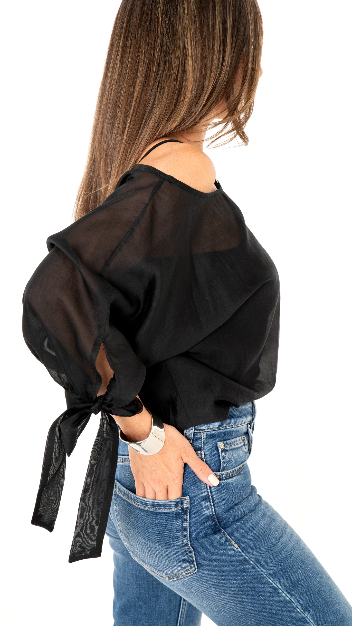 Seitenansicht Damemode: Cooles Outfit aus blauer Jeanshose und weite schwarze Bluse , halbtransparent und Schleifendetail am Ärmel