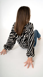 Rückansicht  sitzend feminine Damenmode mit Animal Print: weite Bluse in Zebra Print mit Volumen Arm, kombiniert mit blauer Denim Hose als casual Büro Outfit