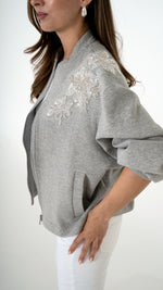 Feminine Damenmode in grau weiß: Model trägt eine coole feminine Sweat Blouson Jacke in grau mit floraler Glitzer Stickerei. dazu trägt sie eine weiße Skinny Denim Hose