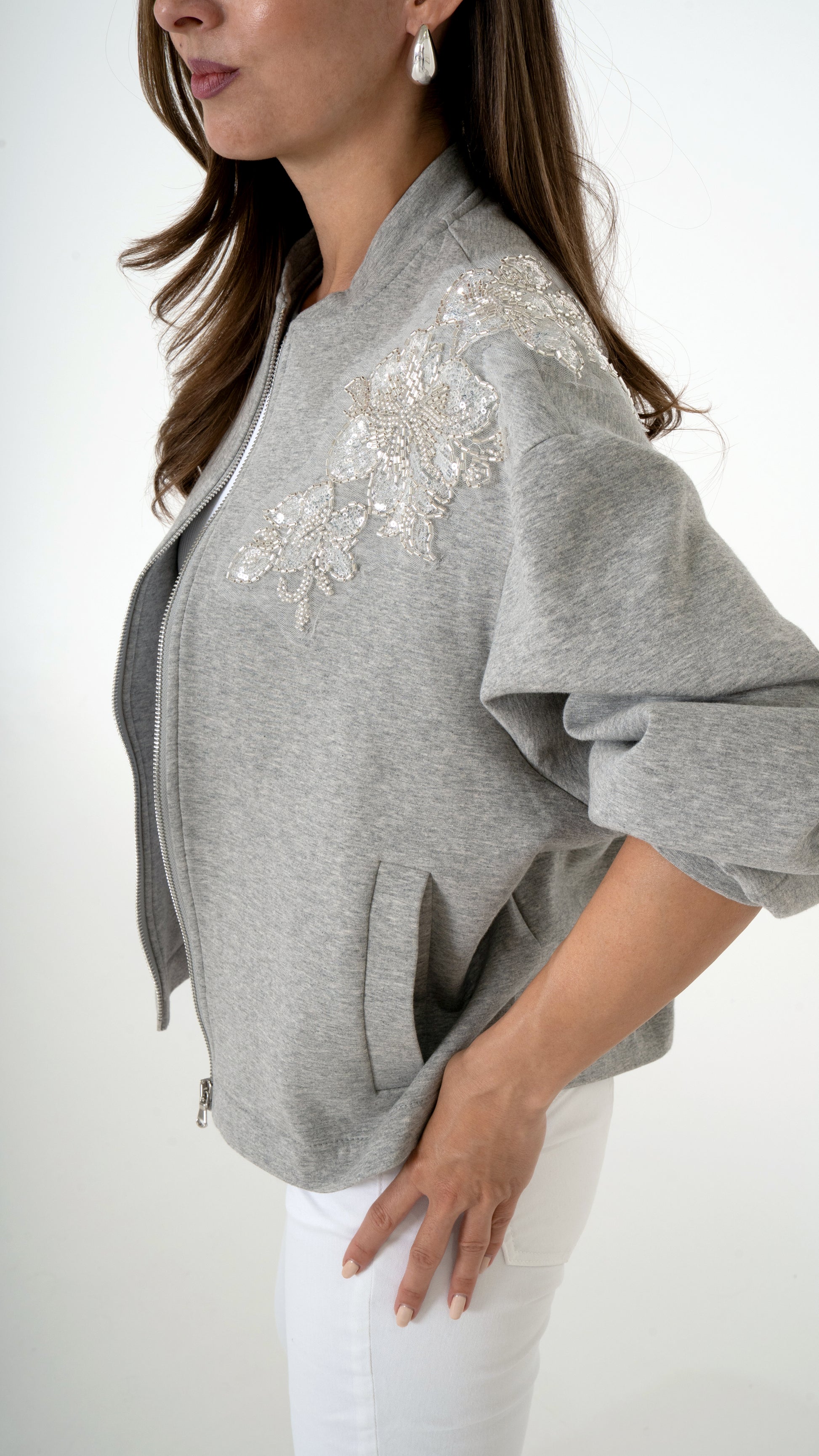 Feminine Damenmode in grau weiß: Model trägt eine coole feminine Sweat Blouson Jacke in grau mit floraler Glitzer Stickerei. dazu trägt sie eine weiße Skinny Denim Hose