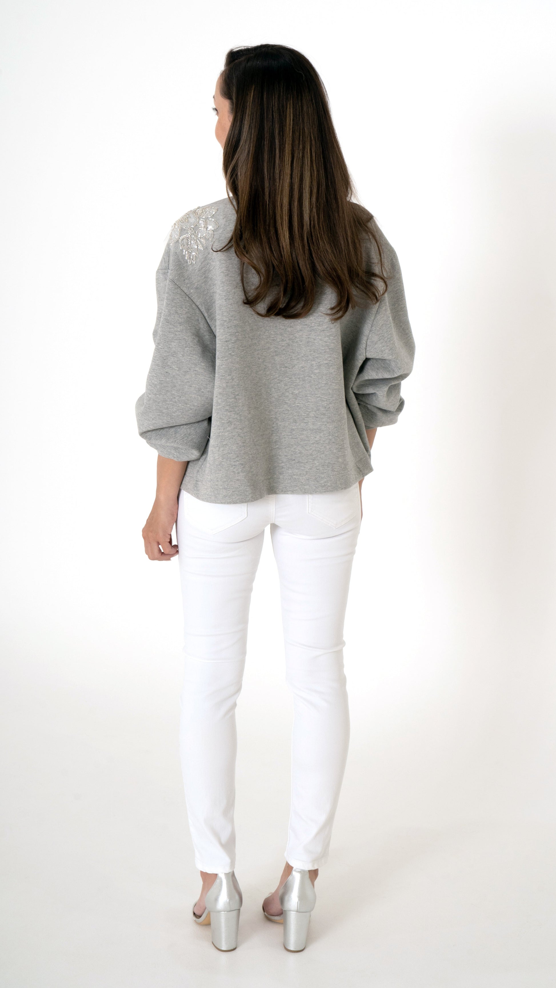 Feminine Damenmode in grau weiß- Rückansicht: Model trägt eine lässige Volumen Sweat Blouson Jacke in grau mit floraler Trend Stickerei. dazu trägt sie eine weiße Skinny Denim und silber metallic Sandaletten