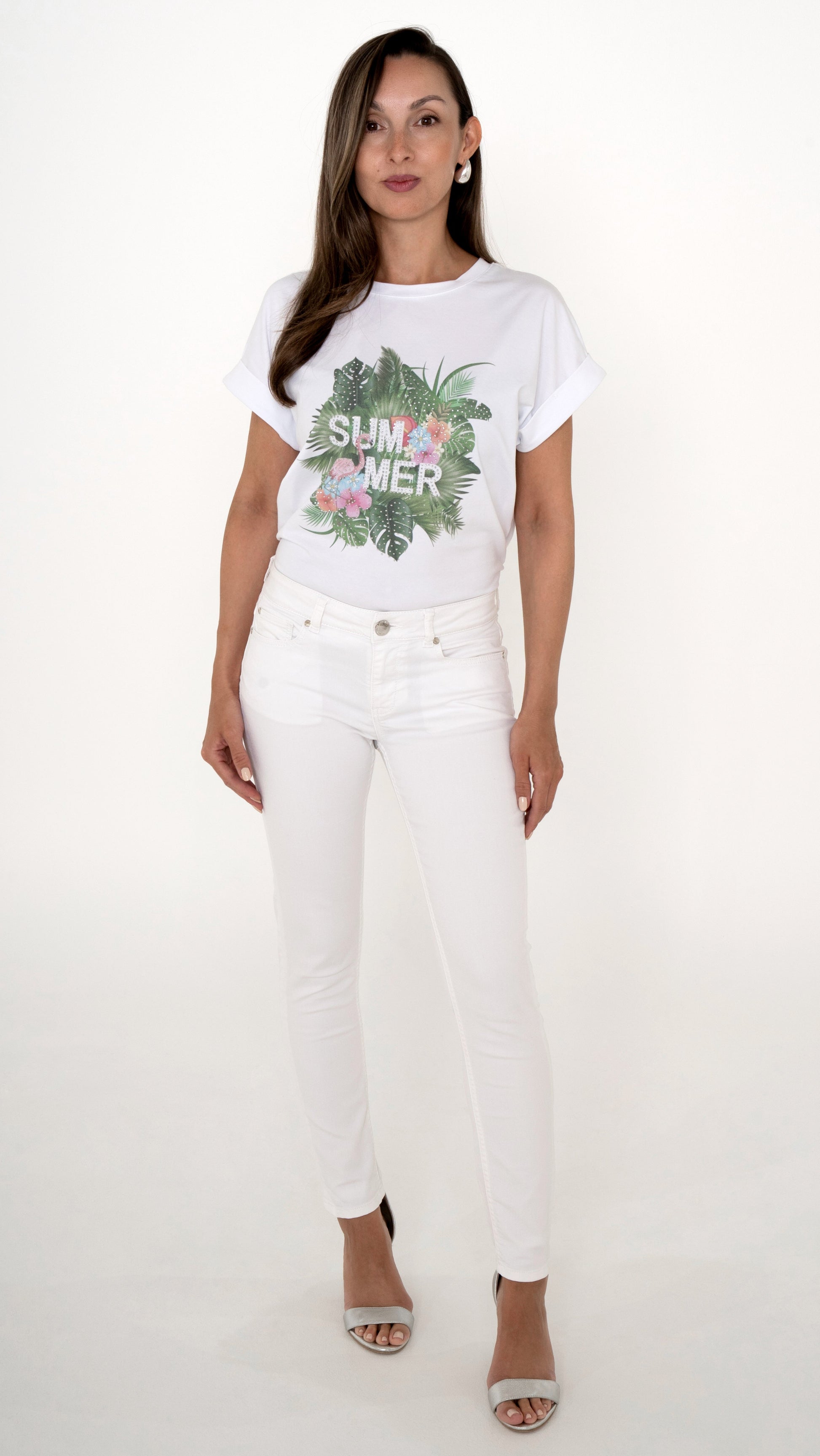 Feminine Sommer Damenmode in weiß: Model trägt ein weißes Outfit bestehend aus einer Skinny Denim Hose in weiß. Dazu ein weißes T-Shirt mit tropischem Sommer-Print mit Palmen und Blumen. Silberne Sandaletten
