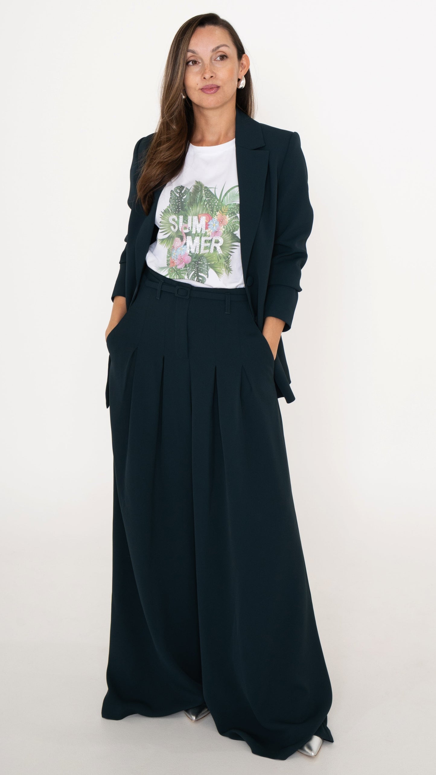 Feminine ausgefallene Damenmodein petrol: Model trägt ein modisdh Business Outfit bestehend aus einem Anzug in Petrol: langes Blazer und eine Hose mit Falten und ultra weitem Bein. Dazu ein weißes T-Shirt mit tropischem Sommer-Print mit Palmen und Blumen. Silberne Pumps