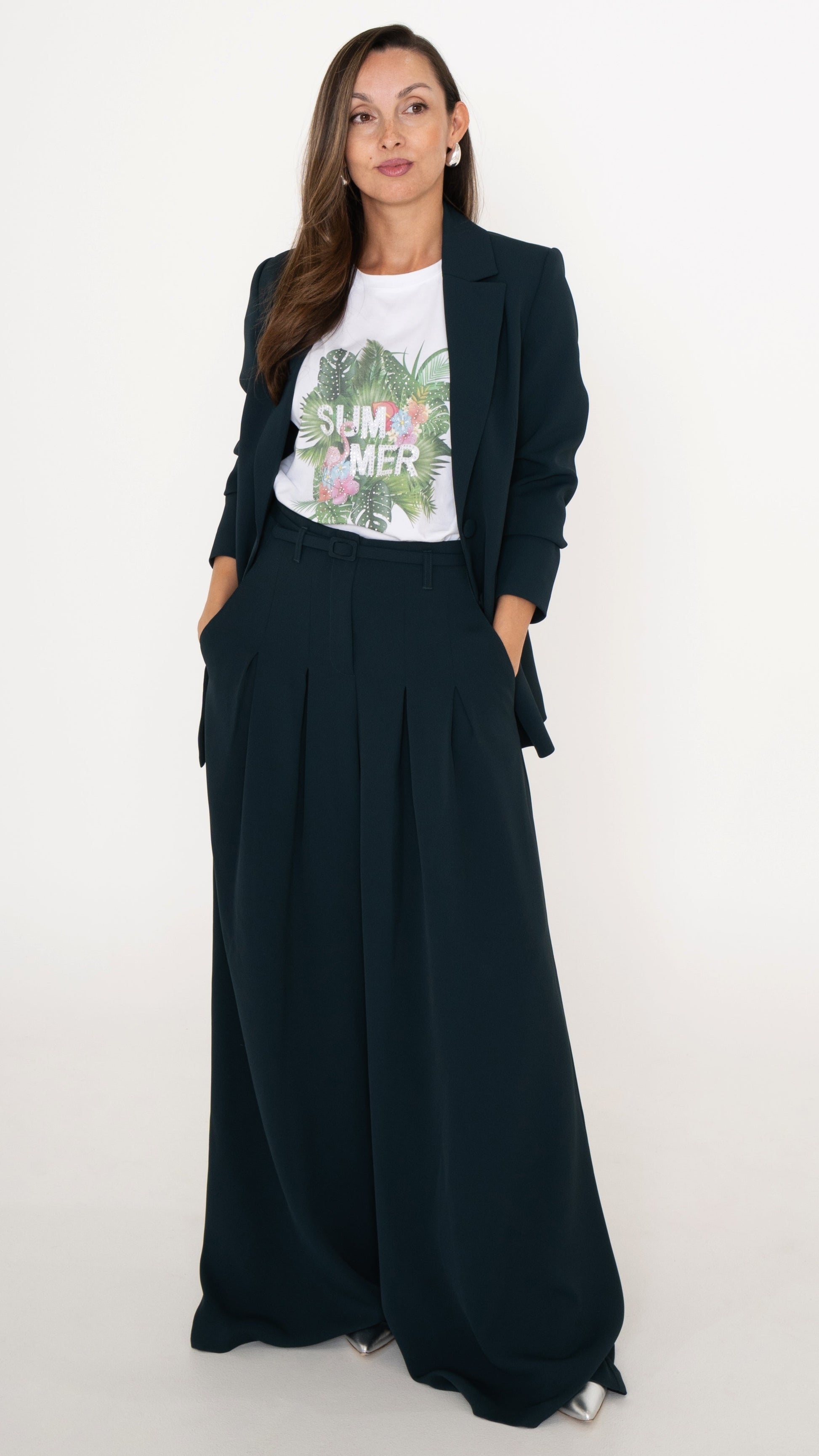 Feminine ausgefallene Damenmodein petrol: Model trägt ein modisdh Business Outfit bestehend aus einem Anzug in Petrol: langes Blazer und eine Hose mit Falten und ultra weitem Bein. Dazu ein weißes T-Shirt mit tropischem Sommer-Print mit Palmen und Blumen. Silberne Pumps