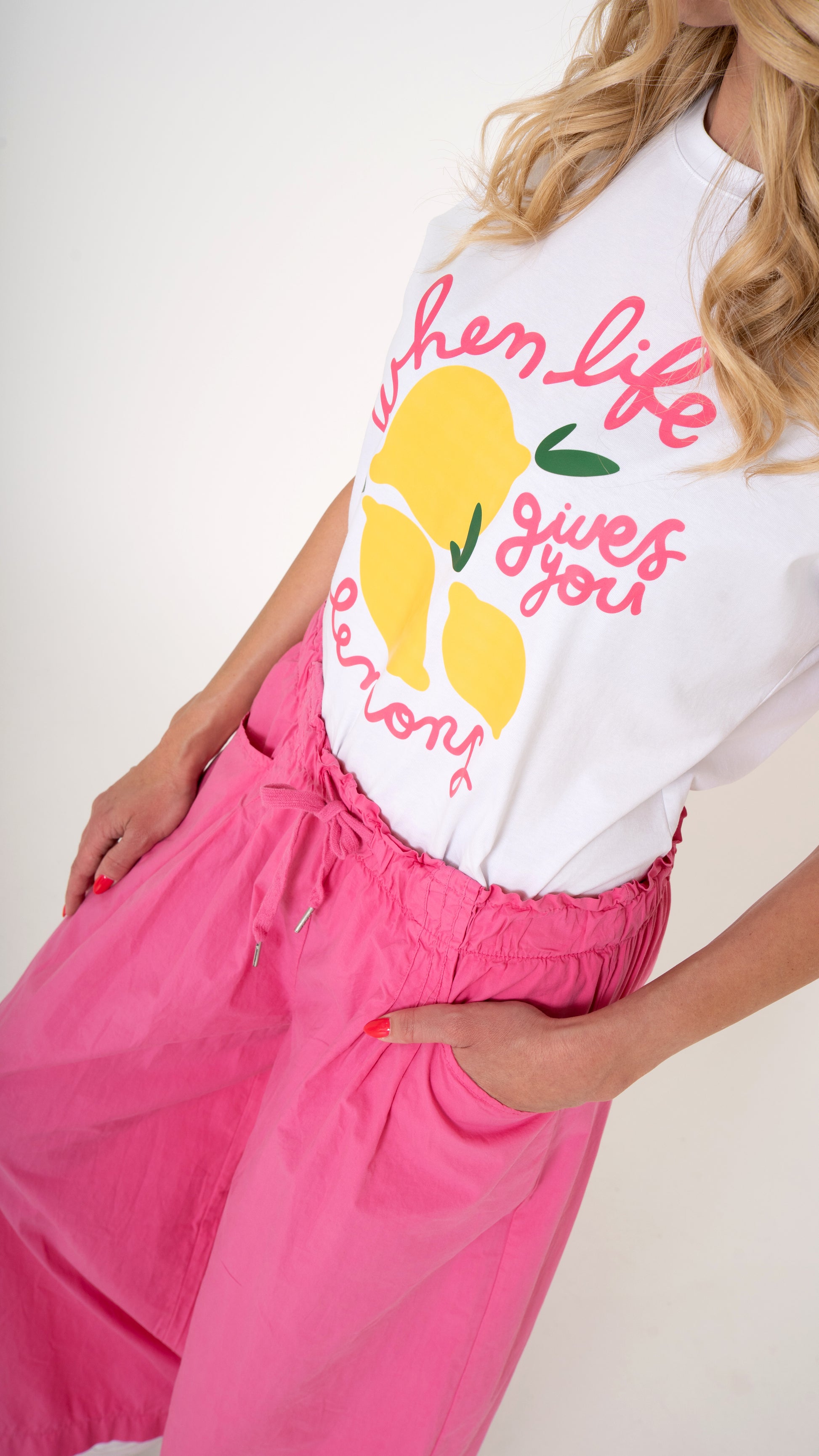 Eine blonde Frau trägt ein cooles lässiges Sommeroutfit: pinke weite Damen Hose mit elastischem Bund und Schleife, lässige Passform. Dazu ein weißes Sommer T-shirt mit Druck aus Zitronen und pinker Schrift