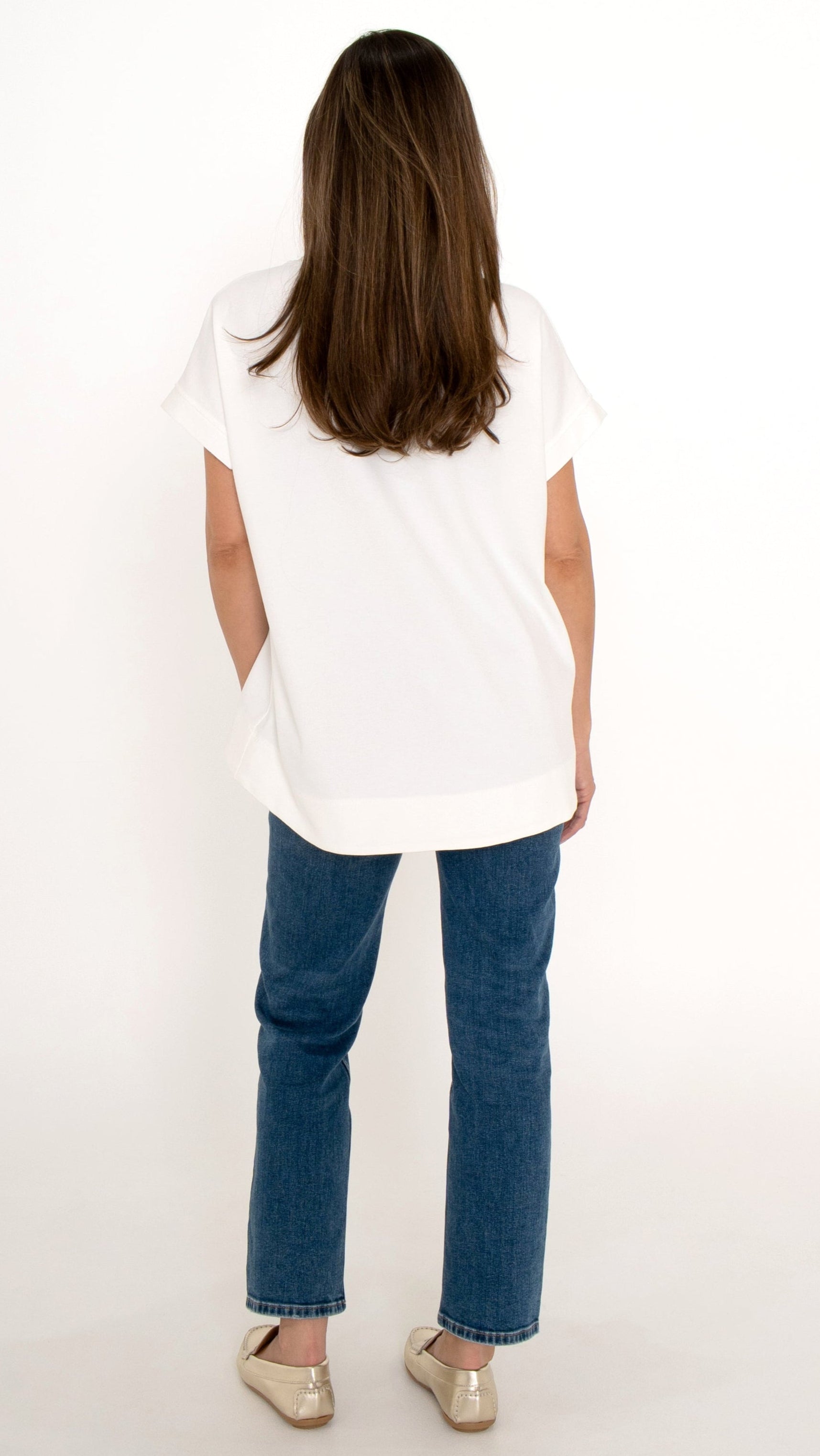 Feminine Damenmode Rückansicht: Model trägt ein feminines Alltagsoutfit bestehend aus einer geraden Denim Jeanshose in blau, goldene Loafer und ein moderne T-Shirt mit lockerer Passform 