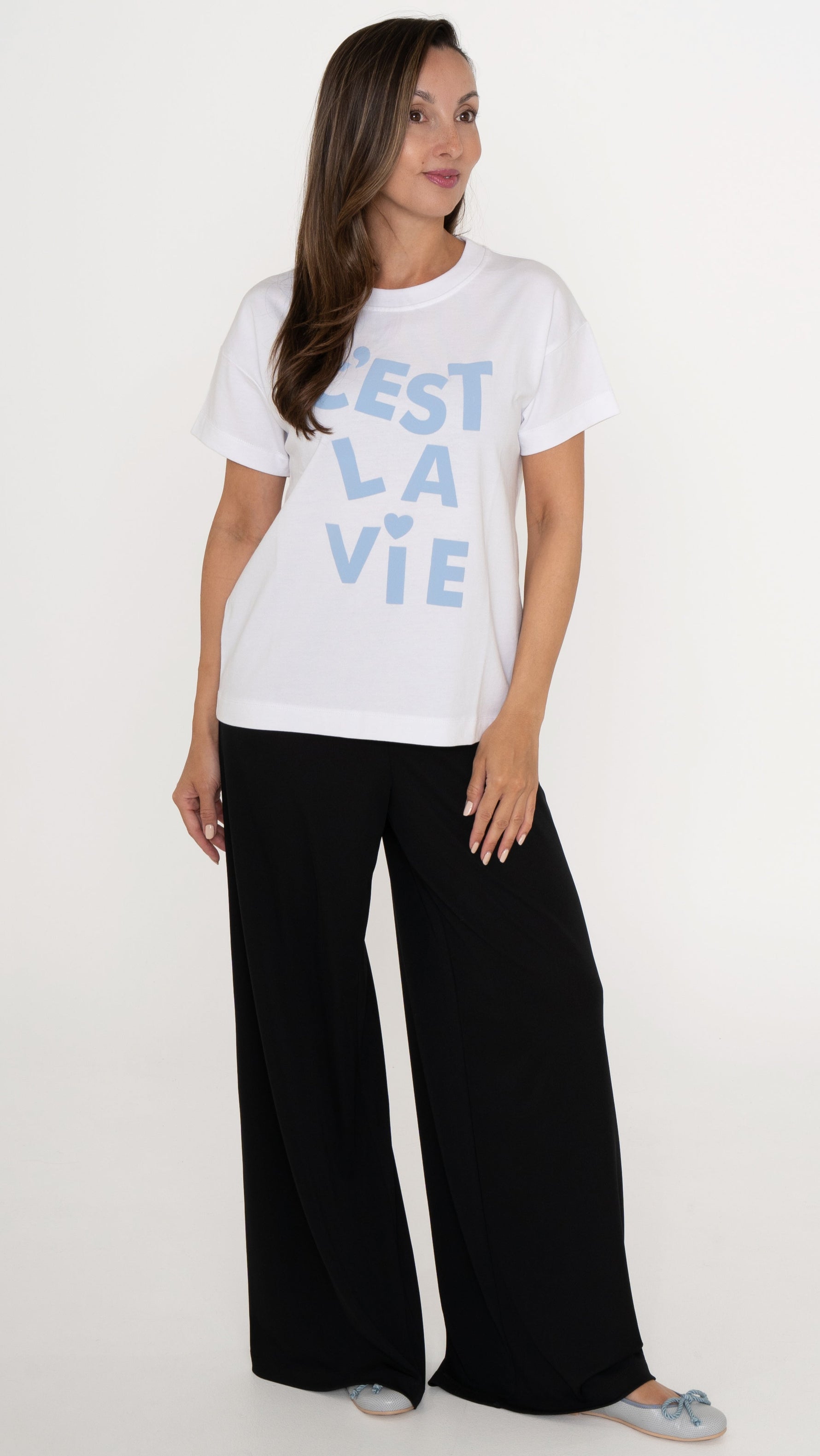 Feminine Damenmode: Model trägt eine schwarze locker weite Hose und ein weißes lässiges T-Shirt mit hellblauer Schrift: C´est La Vie