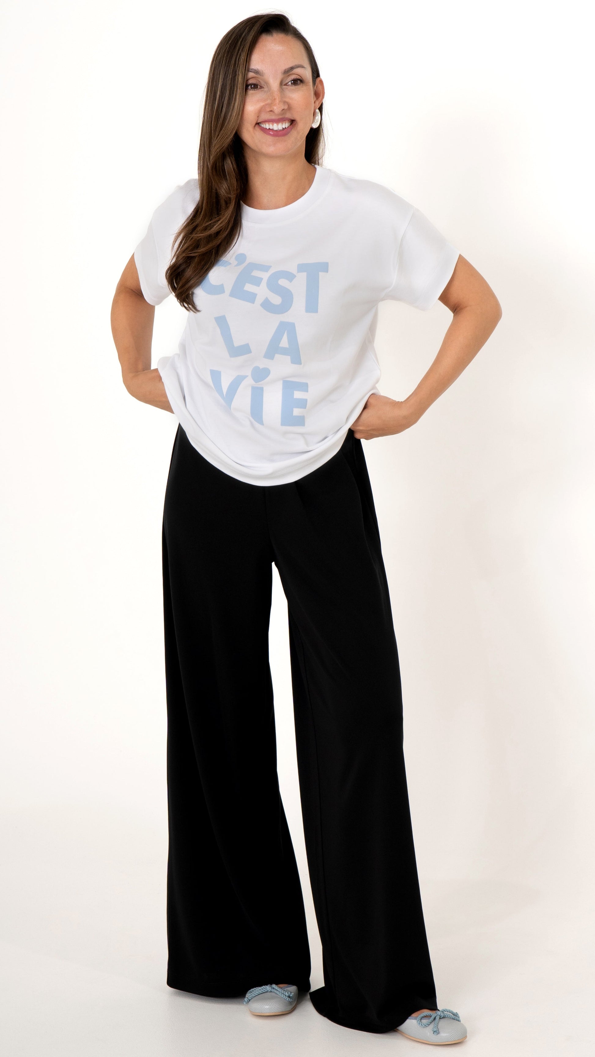Feminine Damenmode: Model trägt eine schwarze locker weite Hose und ein weißes lässiges T-Shirt mit hellblauer Schrift: C´est La Vie