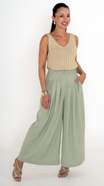 Elegante Damenbekleidung mit einem  ausgefallenen Sommeroutfit. Es besteht aus einer verkürzten Stoffhose mit Falten und extra weitem Bein in einem hellen Maigrün. Das Oberteil ist ein goldenes Stricktop mit leichtem Glanz, ohne Ärmel