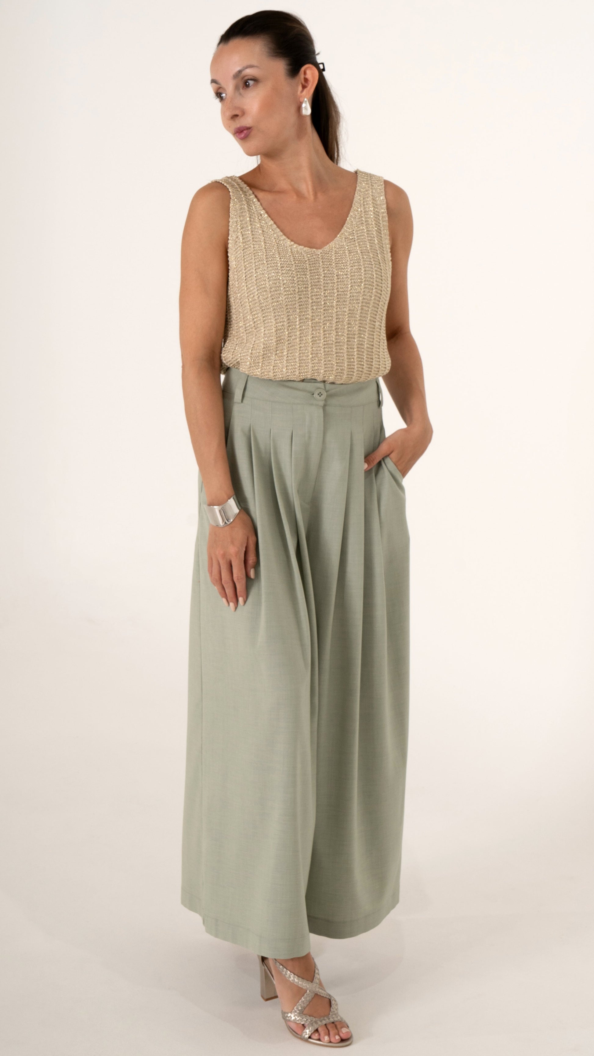 Eine Frau trägt ein sommerlich feminines Outfit bestehend aus goldenem Stricktop ohne Ärmel und einer weiten verkürzten Faltenhose in soft may green