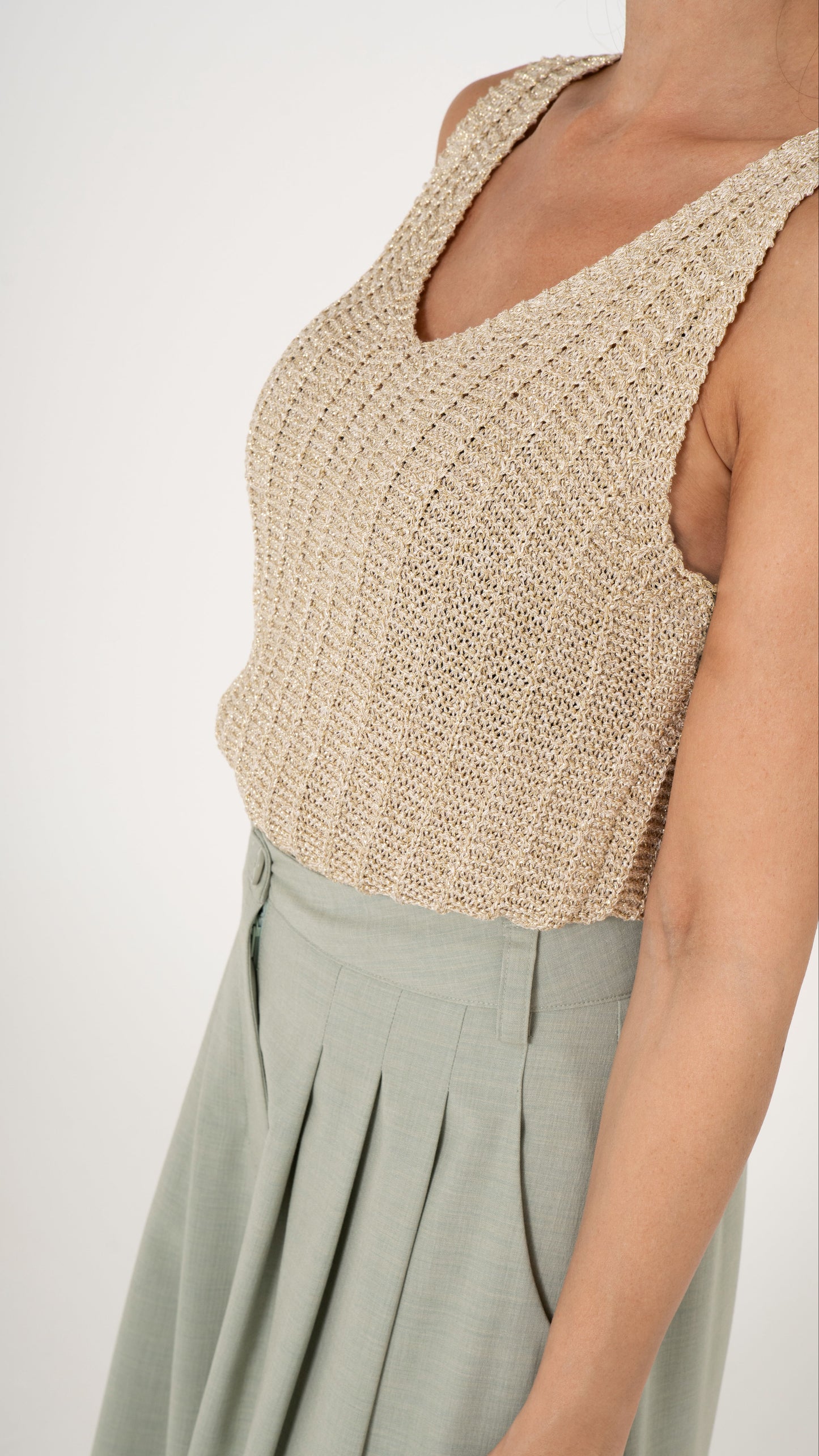 Detailansicvht goldenes Stricktop ärmellos mit V-Ausschnitt. Dazu eine Bundfaltenhose in hellem grün