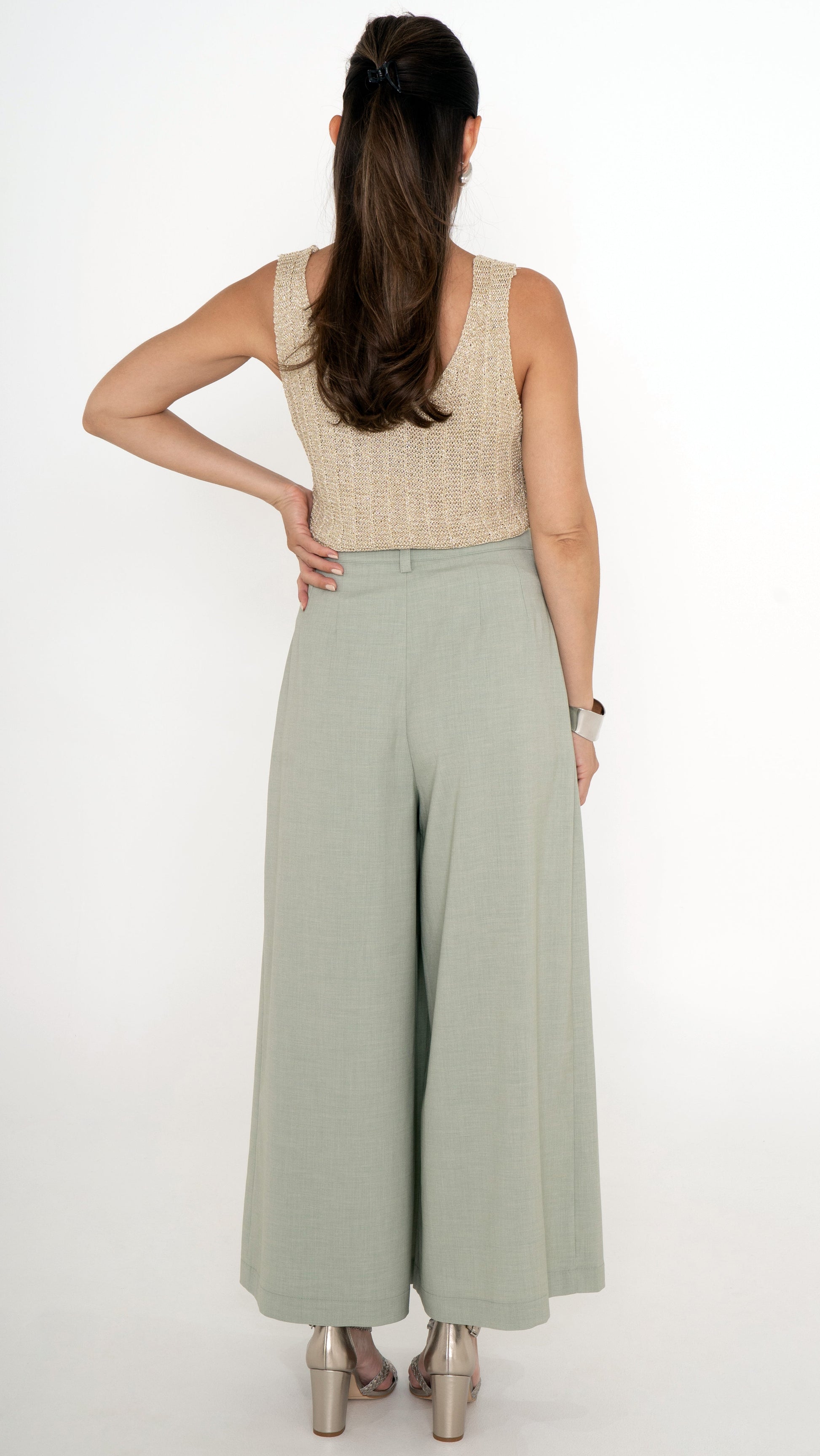 Rückansicht von eleganter Damenbekleidung: Verkürzte Stoffhose mit weitem verkürztem Bein in der Farbe soft may green. Gold Glitzer Stricktop ohne Ärmel und tiefem Rückenausschnitt