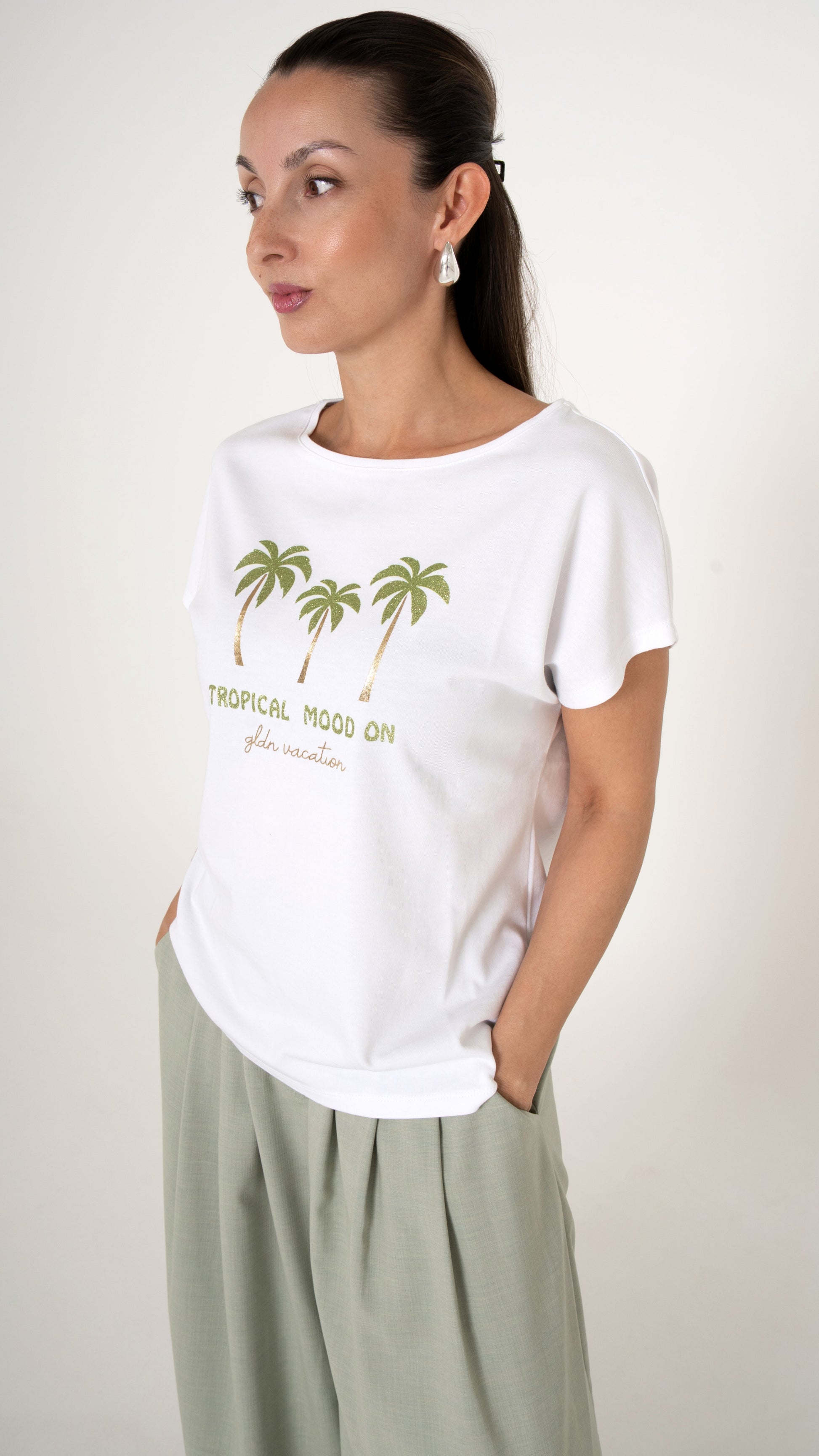Detailansicht: ein Model trägt ein weißen T-Shirt mit tropischem Palmenprint mit Gold und Glitzer.