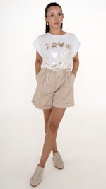 Model in femininer Damenmode für den Sommer: das Model trägt ein sommerlich schickes Outfit bestehend aus einer beigen weiten Short mit Falten sowie einem weißen T-Shirt mit goldener Schrift: metallic Druck