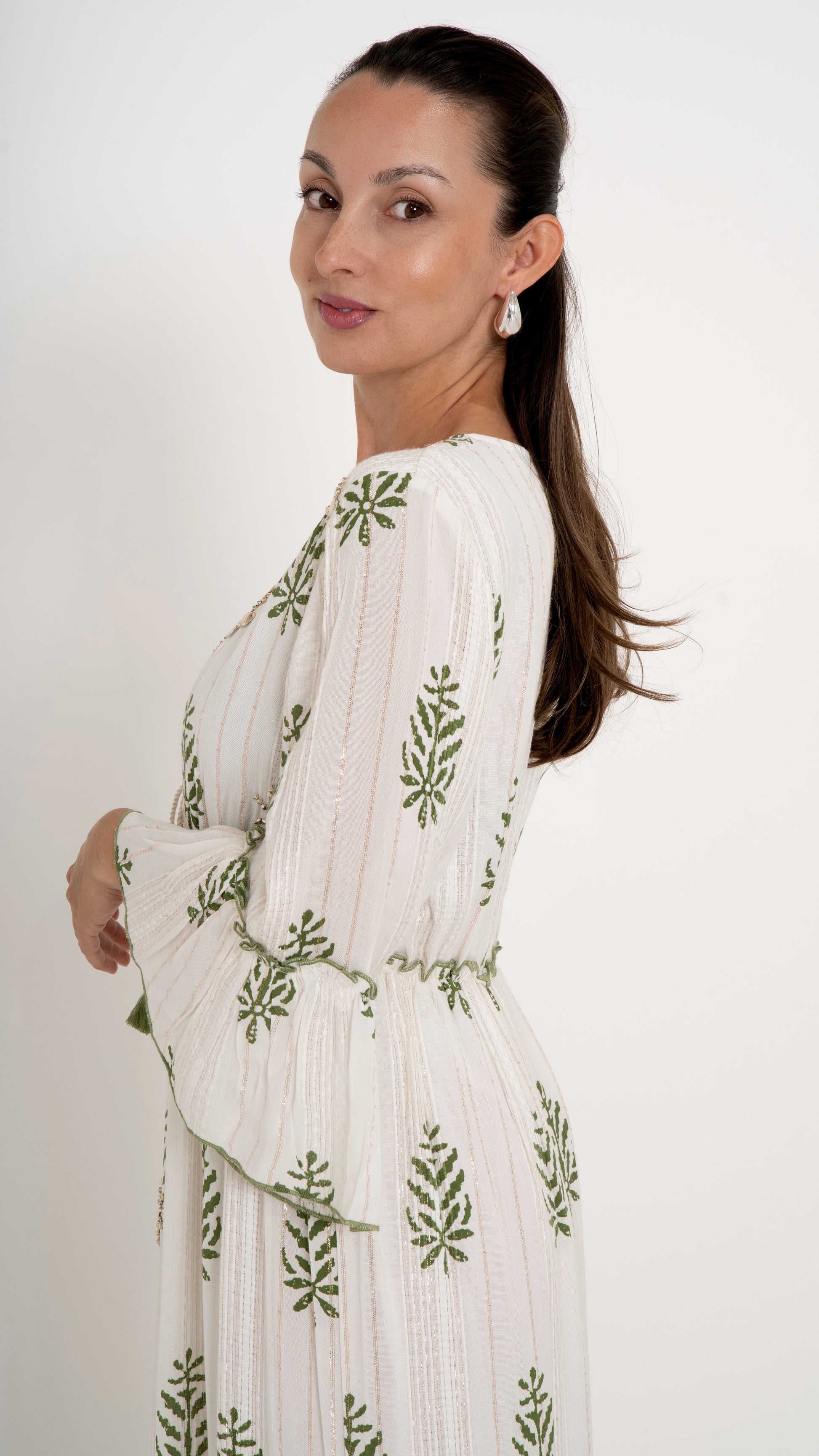 Seitenansicht Feminine Damenmode für den Sommer: Bohemian Maxikleid in offwhite mit floraler Stickerei in Pine green, Trompetenarm, Stufenkleid mit Rüschen, Gold Glitzer Metallic Details